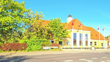 Ein Gebäude mit gelber Fassade und rotem Dach, eine Fahrradspur und ein klarer, blauer Himmel.