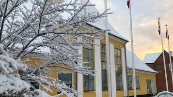 Un edificio amarillo con techo nevado y asta de banderas.