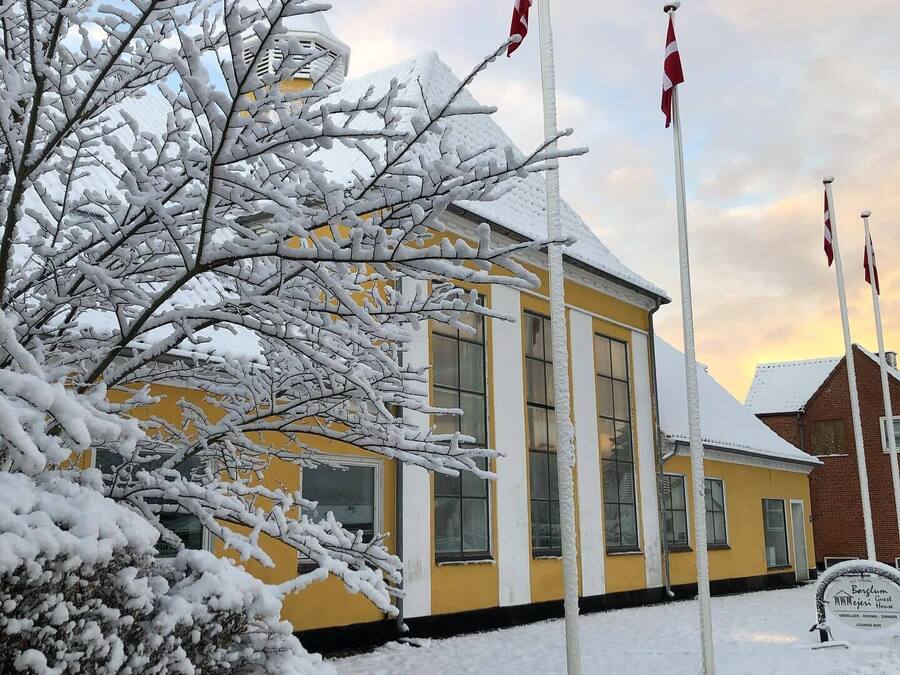 Un edificio amarillo con techo nevado y asta de banderas.