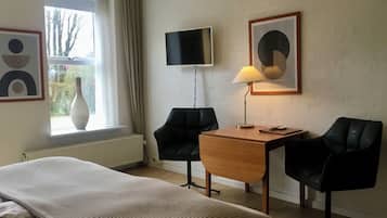 Ett hotellrum med en säng, ett skrivbord med två stolar, en tv och konstverk på väggarna.