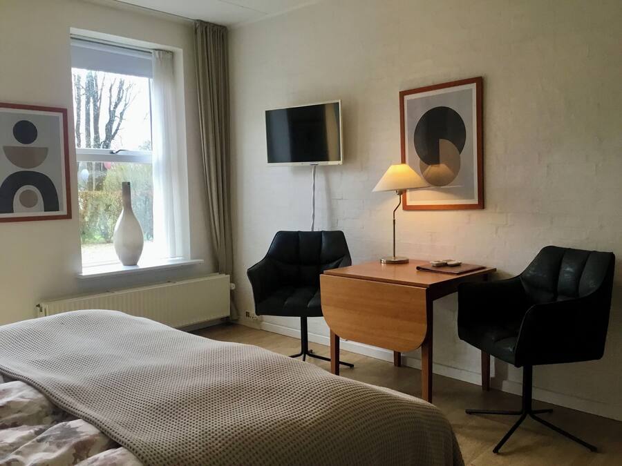 Ett hotellrum med en säng, ett skrivbord med två stolar, en tv och konstverk på väggarna.