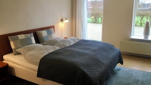 Un dormitorio con cama, almohadas, lámpara de noche, ventana y radiador.