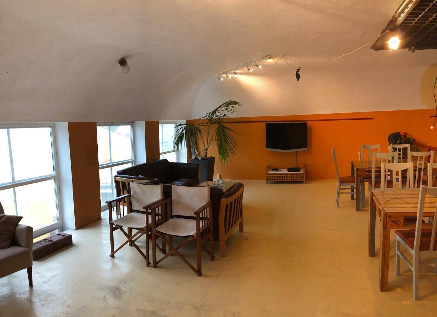 A spacious living area with a sofa, chairs, a dining table, and a TV mounted on the wall.