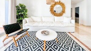 Un salon moderne avec un canapé blanc, un tapis à motifs noir et blanc, une table basse ronde et un fauteuil rayé noir et blanc.