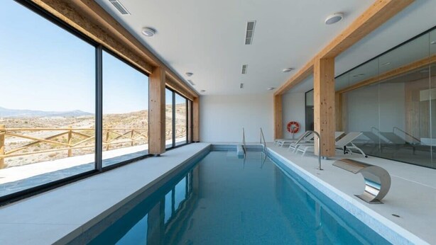 Une piscine intérieure moderne offrant une vue dégagée sur un paysage désertique grâce à de grandes fenêtres.