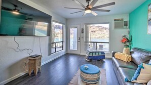A living room with a dark wood floor, a ceiling fan, a blue van toy, a brown leather couch, and a window with a mountain view. - Parker Studio Nestled on the Colorado River! (Parker)