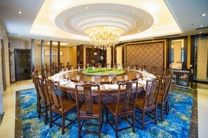 Een ronde eettafel met stoelen, een kroonluchter en een blauw tapijt.