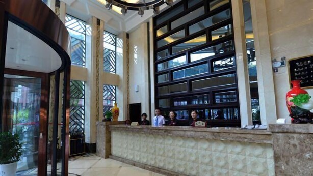 Un hall de hotel con mostrador de recepción, ventanas amplias y un jarrón decorativo.