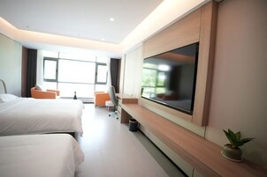 Una habitación de hotel moderna con dos camas, un televisor grande, un escritorio y una ventana.