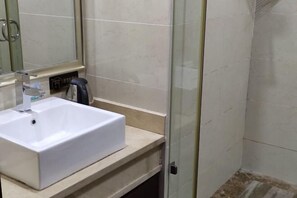 Un baño con lavamanos blanco, un espejo y zona de ducha.