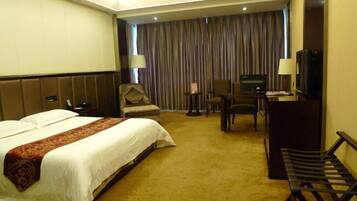 A hotel room with a large bed, a desk, a chair, a television, and a bench.