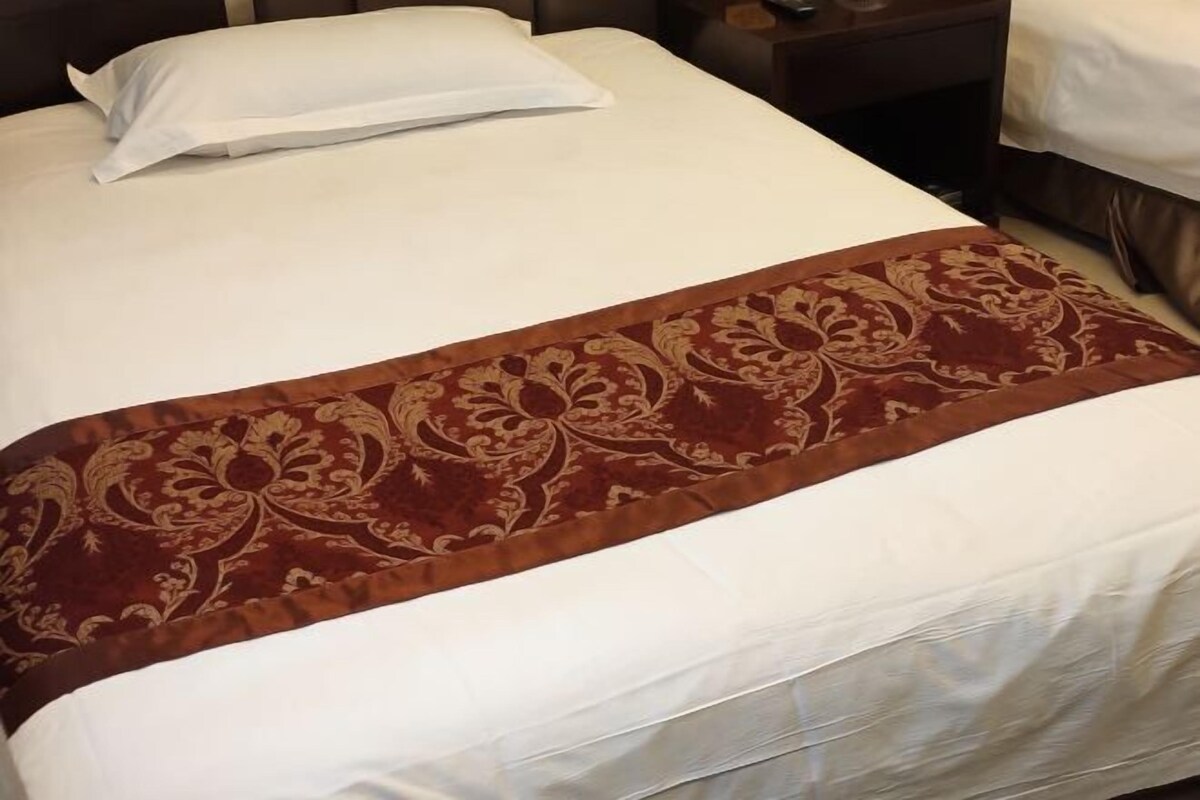 Una cama bien hecha con sábana blanca y un corredor decorativo marrón.