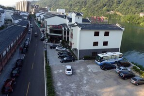 Un estacionamiento con varios coches y un autobús, un edificio de techo plano y un río al fondo.
