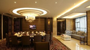 Una habitación de hotel moderna con comedor, sala de estar con sofá y televisor, y un candelabro.