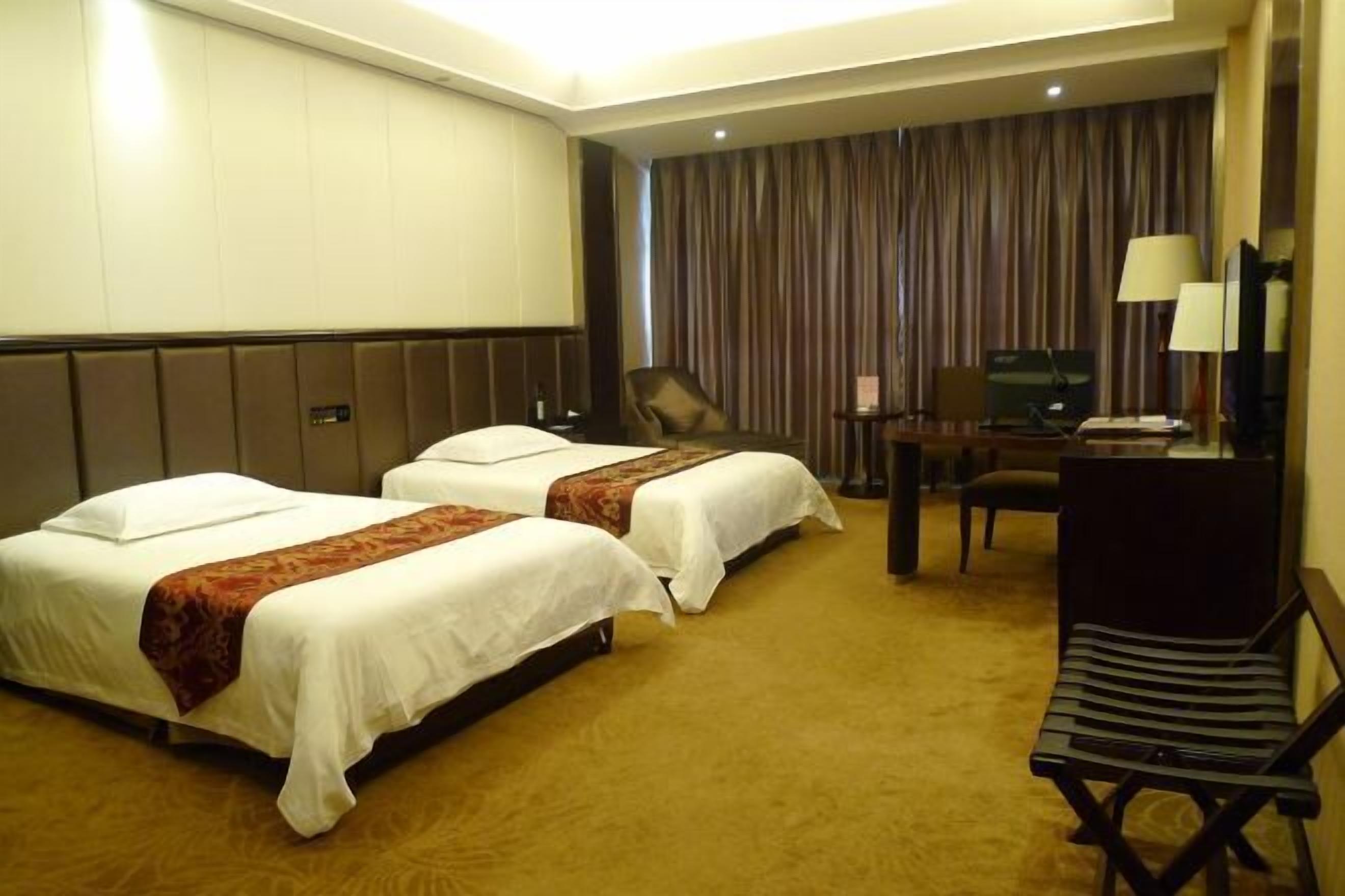 A hotel room with two beds, a desk, a chair, a television, and a lamp.