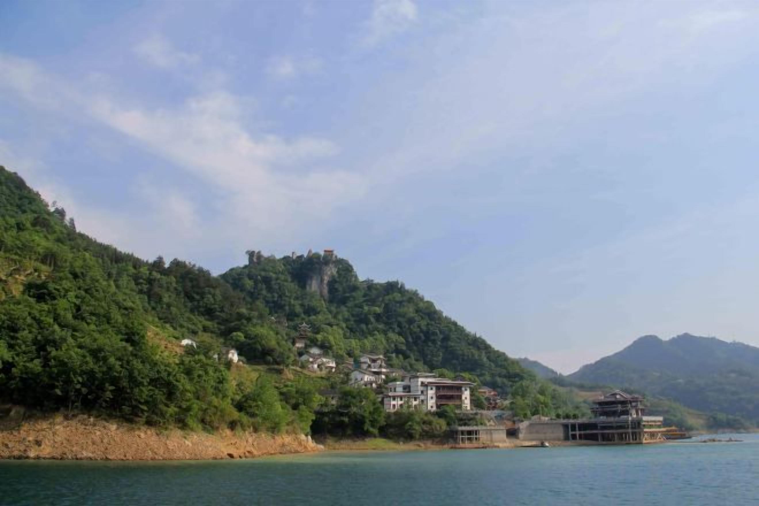 A coastal landscape with buildings on a hillside, a body of water, and a distant mountain range.