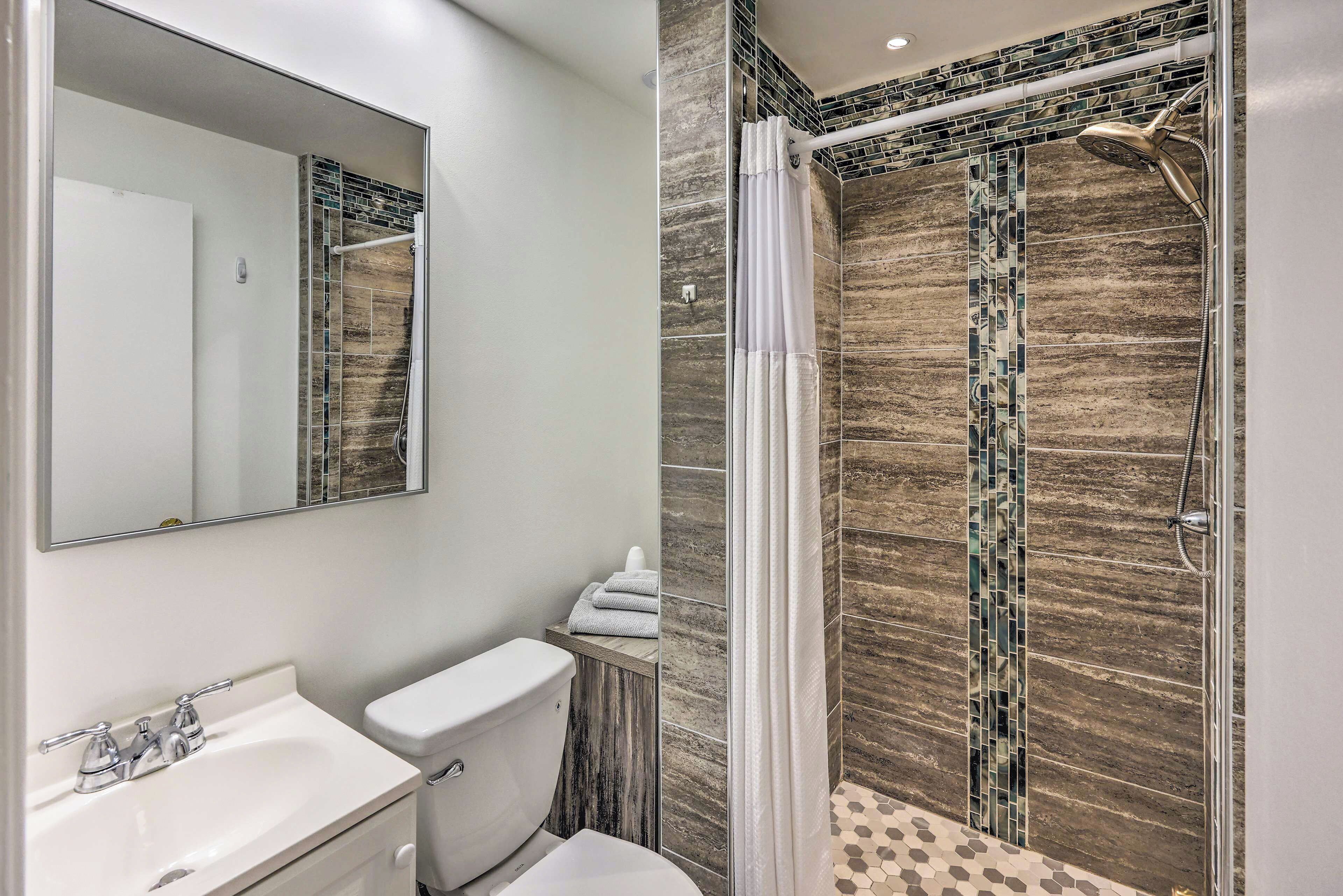 A bathroom with a shower, toilet, sink, and a mirror.