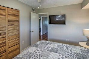 Une chambre à coucher comprenant un lit, une armoire en bois, un téléviseur fixé au mur et une porte donnant sur une autre pièce.