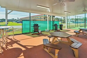 Un espace extérieur aménagé en terrasse, avec des tables de pique-nique et des barbecues, le tout délimité par une clôture en treillis métallique.