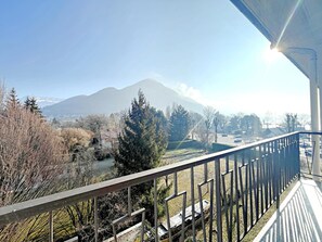 A balcony with a metal railing overlooking a mountainous landscape and a parking area.