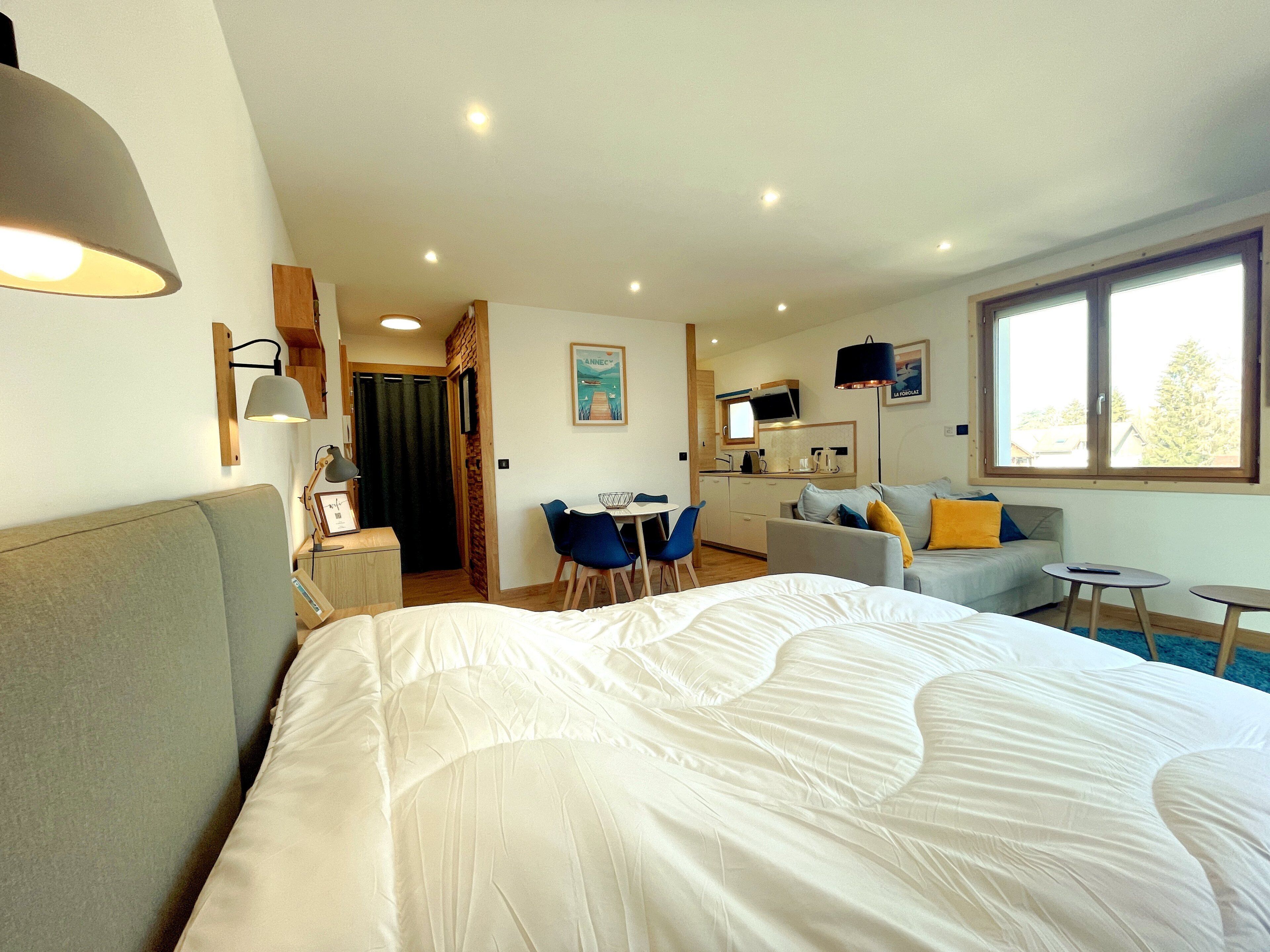 A hotel room with a large bed, a desk, a sofa, and a window with a view.