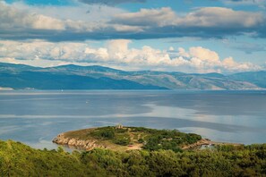 Un paysage côtier avec une petite île, des montagnes lointaines et un ciel dégagé.