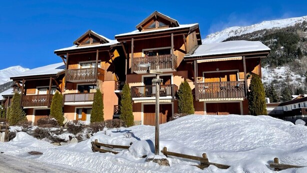 A multi-story wooden lodge with balconies, set against a snowy mountain backdrop.