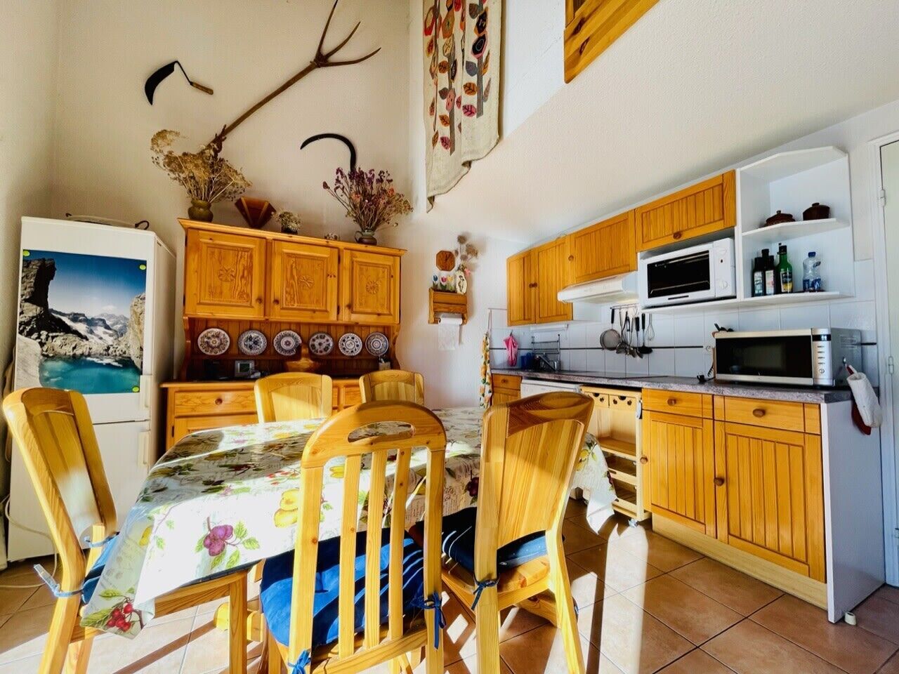 Une cuisine de taille réduite, dotée de meubles de rangement en bois, d’une table à manger avec des chaises et d’un réfrigérateur.