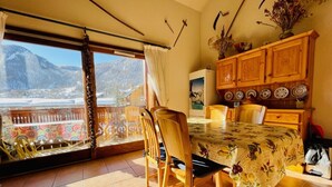 A dining area with a table and chairs, a view of mountains through a large window, and a wooden cabinet with decorative plates.