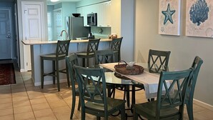 A dining area with a glass table and chairs, a chandelier, and artwork on the walls. - Pearl 1003 Sugar white sand and emerald waters (Navarre)