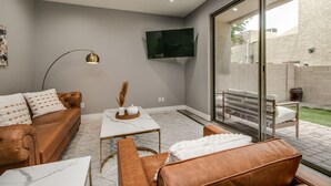 Een moderne woonkamer met een bruine leren bank, een witte salontafel en een grote televisie aan de muur.