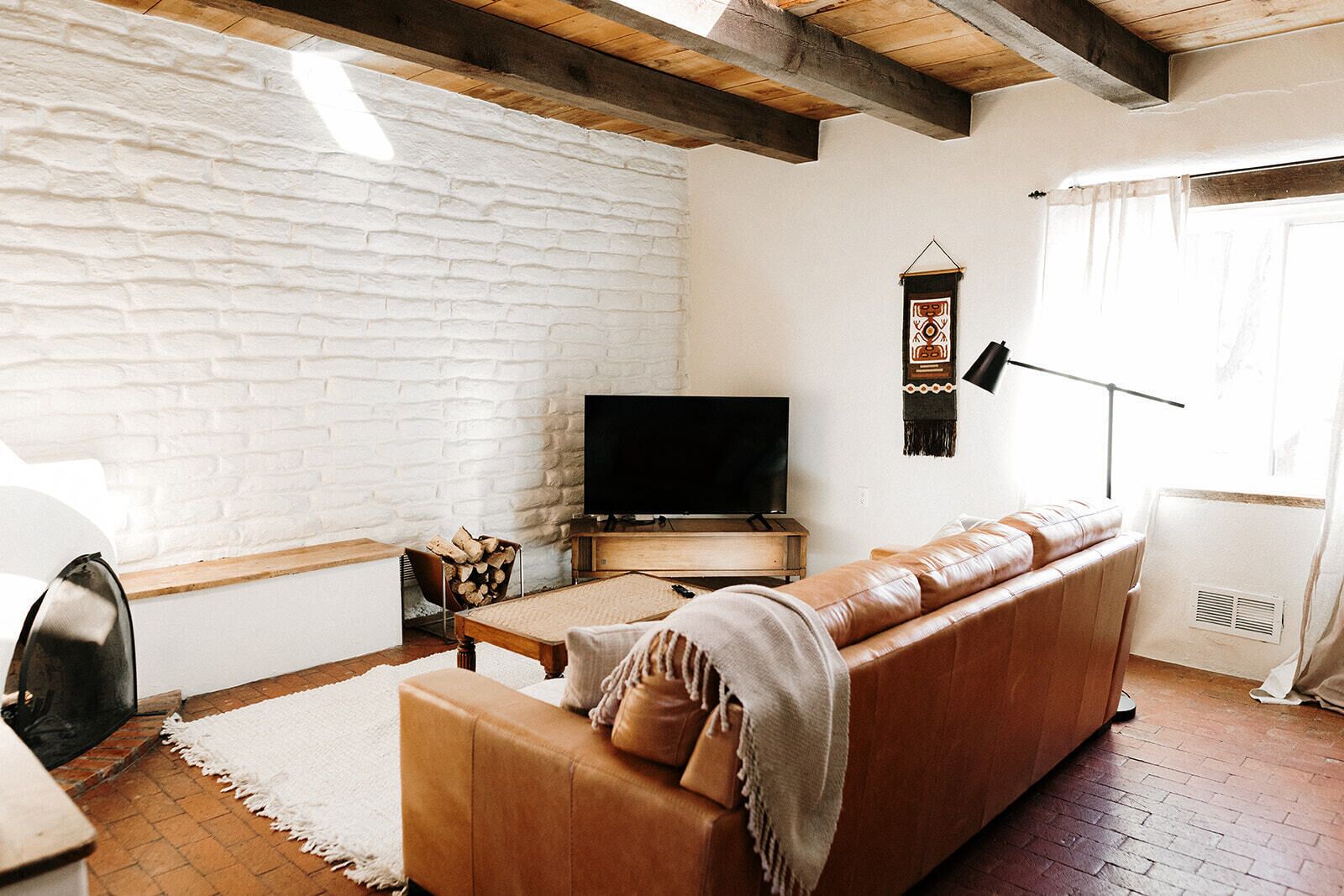 Ein Wohnzimmer mit weißer Ziegelwand, einem Ledersofa, einem Fernseher, einem Kamin und einem Fenster mit Vorhängen.
