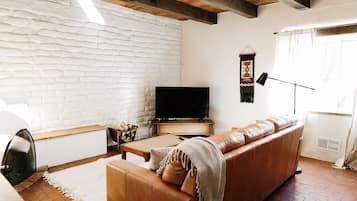 Ein Wohnzimmer mit weißer Ziegelwand, einem Ledersofa, einem Fernseher, einem Kamin und einem Fenster mit Vorhängen.