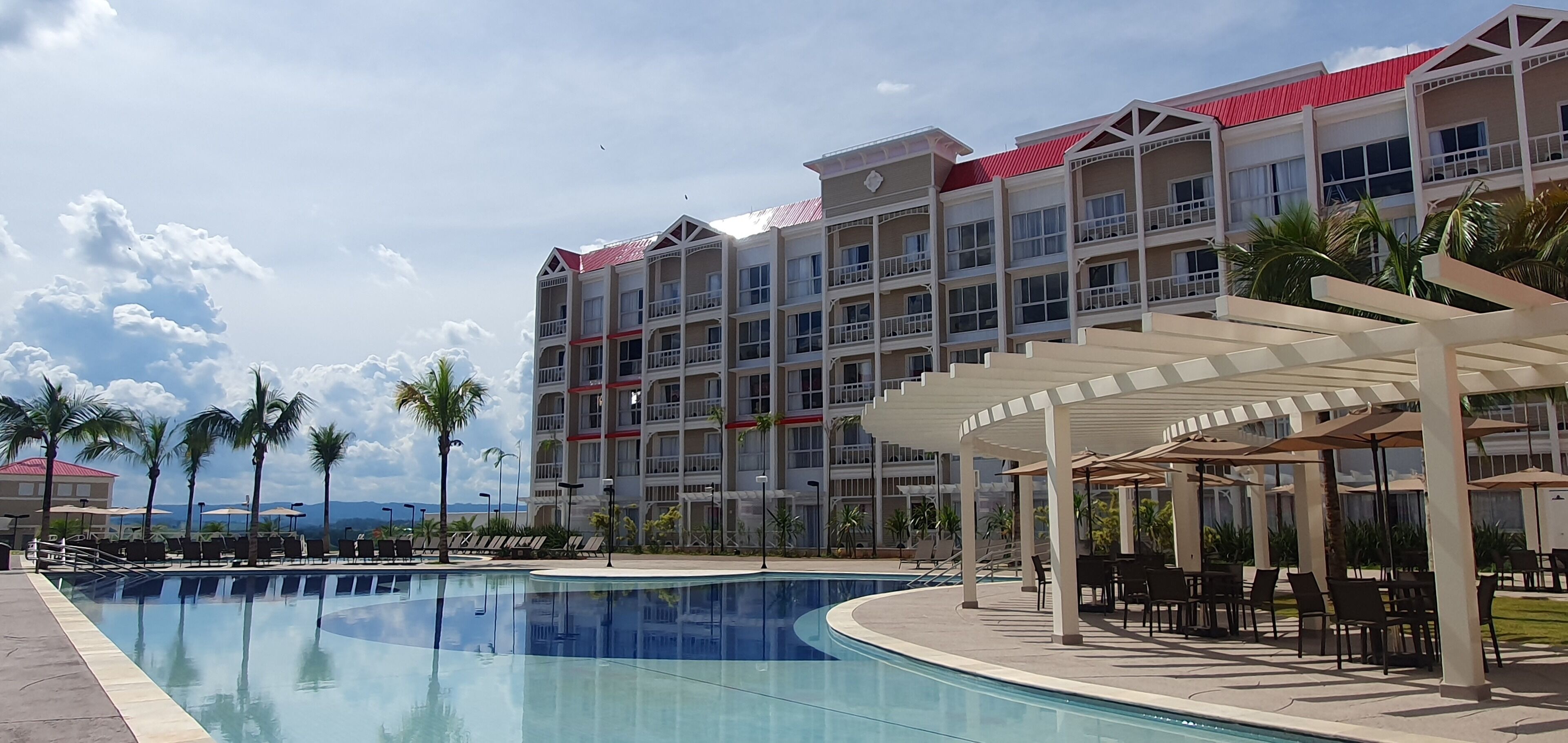 Un hotel con piscina, mobiliario exterior y un edificio de techo rojo.