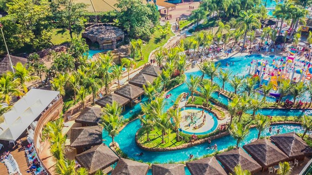 Ein Resort mit mehreren Schwimmbecken, Palmen und strohgedeckten Gebäuden.