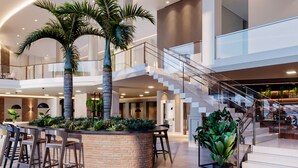 Eine geräumige Lobby mit einer zentralen Sitzecke, Palmen und einer Treppe, die mehrere Etagen verbindet.