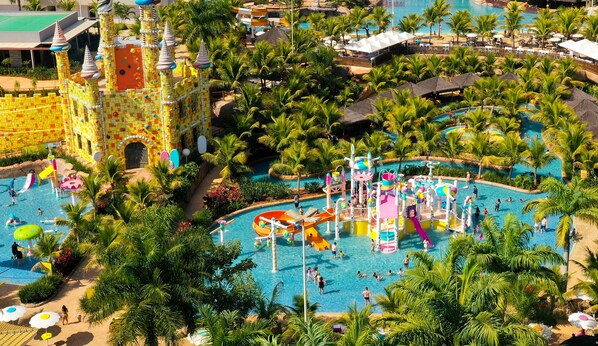 Parque acuático con múltiples piscinas, toboganes y estructuras de juego rodeado de palmeras.