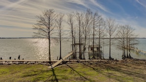 A lakeside view with a wooden dock, a small wooden structure, and leafless trees.