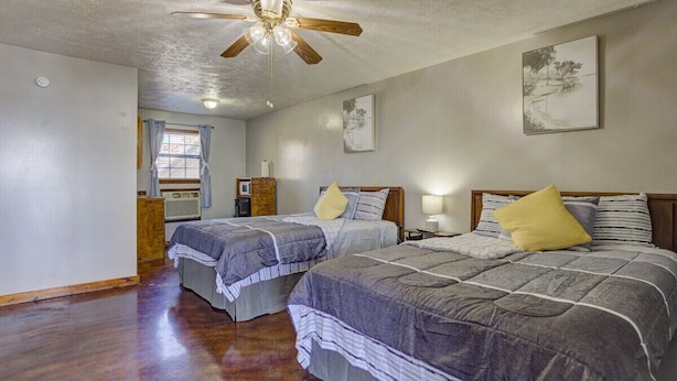 A room with two beds, a ceiling fan, a window with curtains, and a wall-mounted picture.