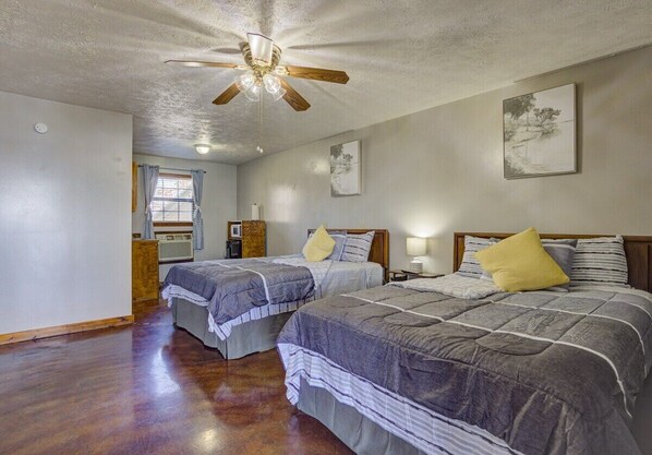A room with two beds, a ceiling fan, a window with curtains, and a wall-mounted picture.