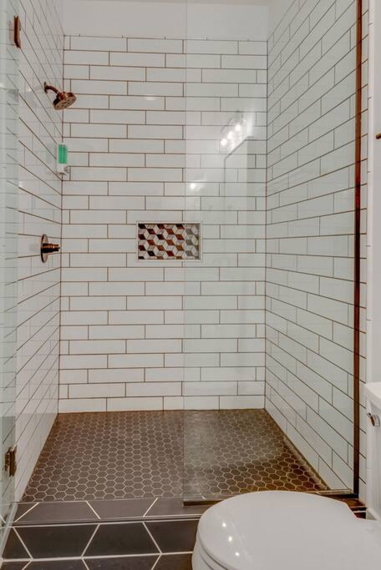 Un espace douche avec des carreaux de céramique blancs rectangulaires et un sol carrelé à motifs hexagonaux.