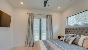 A bedroom with a large bed, a headboard, a nightstand, and a window with blinds.