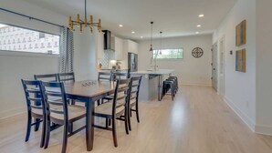 A modern kitchen with a central island, dining area with chairs, and a large window.