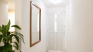 Un pasillo con una planta en maceta, un espejo y una puerta blanca con reja de metal.