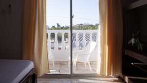 Una habitación con cama, puerta corrediza de vidrio a un balcón y una planta en maceta.