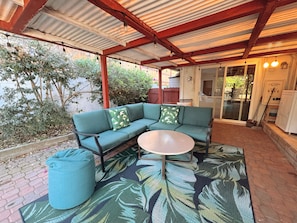 A covered patio area with a sectional sofa, a round table, and a matching ottoman.
