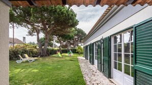 A covered patio with a neatly trimmed lawn, a children's play area, and a house with green shutters. - Miro Villa, Meco, Sesimbra (Sesimbra)
