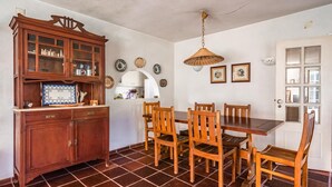 A dining area with a wooden table and chairs, a cabinet with glass doors, and a hanging lamp. - Miro Villa, Meco, Sesimbra (Sesimbra)
