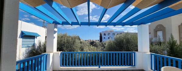 A covered outdoor area with blue railings and a view of buildings in the background. - Stunning villa in a tourist area (Hammamet)