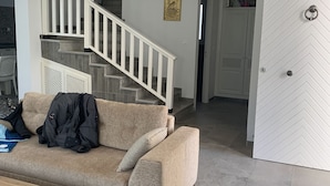Una sala de estar moderna con un sofá color crema, una mesa de centro de madera y una escalera con barandillas blancas.